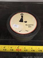 Photo of coaster round box containing set, showing 'Shopping Girl' woman with basket on cover