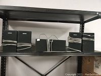 Five Sony surround speakers shown lined up on a metal shelf, all wired and labeled with Sony logos.