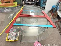 Red framed vintage buck saw lying on a glass table, showing the dimensions with a yardstick. Features curved top with blue tension rod and blue blade with large teeth.