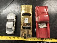 Top view of three vintage metal toy cars shown with a measuring tape for scale