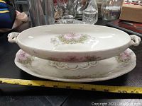 Oval tureen placed inside matching serving dish, both decorated with floral designs, shown with measuring tape for size reference.
