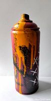 Side view of spray can showing yellow-orange drip paint with black and white graffiti marks on dark purple background