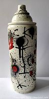 Front view of the painted spray can showing black and red abstract art on cream background