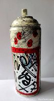 Front view of spray paint can artwork with white base, black splatter, red dots, red framed panel with graffiti style markings.