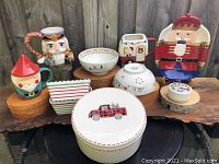 Full view of all 10 items displayed on wooden stands against a wooden fence: nutcracker plate, two striped Crate & Barrel dishes, Christmas Wish bowls, elf coffee mug, nutcracker mug, Santa in RV mug, Hallgem serving tray, Villeroy & Boch trinket dish, 10 Strawberry Street cookie jar