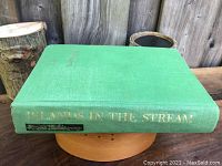 Photo of the green cloth hardcover book raised on a small wooden stand. Spine visible with gold title and author text.
