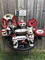 Full collection displayed outdoors on a table against wooden fence, showing all 23 pieces including teapot, dog cookie jars, various plates and trays, and decorative sign