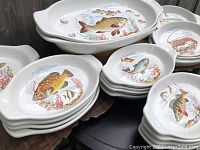 Set of heavy transferware platters stacked and arranged showing fish and lobster illustrations on white ceramic base.