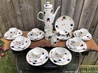 Full set arranged on wooden surface showing coffee pot, creamers, teacups, saucers and salad plates with colorful polka dots and gold accents.