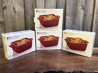 Four boxed Maxwell Williams Chef du Monde square bakers in red, showing front of packaging with baked dish image.