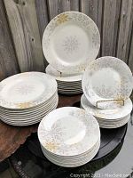Photo showing stacks of 20 large dinner plates and 20 smaller salad plates arranged on a table outdoors against a wooden fence.