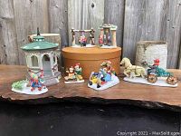 Seven miniature pieces displayed on wooden surface, including pergola, sleds with children, horse-drawn carriage, and figures with Christmas tree.