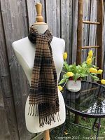 Scarf displayed on a mannequin outdoors with a wooden fence background, showing full length and styling.