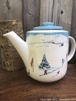 Front and side views showing the winter ski hill design with skiers and a Canadian flag, and the lid with light blue color.