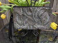 Front view of the Kenneth Cole Reaction beaded leather clutch showing intricate bead and rhinestone design with attached black leather wrist strap.