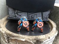 Pair of Marvel Captain America cufflinks displayed on a surface, showing detailed enamel design with Captain America character and shield.