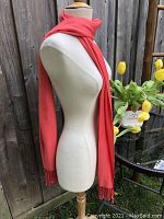 Coral wrap scarf displayed on a dress form showing length and fringe detail