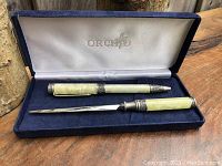 Overview of pen and letter opener inside blue velvet-lined Orchid branded box, showing pearlescent handles with pewter detailing.