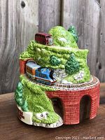 Front view of the porcelain musical figurine featuring Thomas the Train exiting a tunnel on a green hill with a red bus on top.