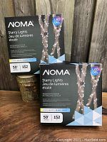 Two unopened boxes of NOMA Starry Lights 50-foot LED light strings on wood surface.