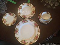 Two place settings including dinner plates, salad or soup plates, teacups, and saucers arranged on a dark surface showing floral bone china with gold trim.