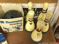 Five Brunswick bowling pins arranged in a group on a wooden surface next to a cardboard box holding a bowling ball