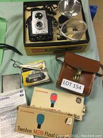 Full view of Brownie Starflex camera with flash unit in original box, leather case, manual, and flashbulb boxes laid out.