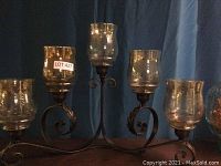 Full view of the 5-shade curved metal candelabra with glass shades on a dark wood surface in front of a curtain