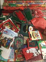 Top view showing folded Christmas gift bags, small gift bags with varied holiday images including snowmen and cardinals, and decorative bows lying on top.