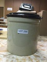 Front view of beige ceramic crock with lid and LOT 294 label on front