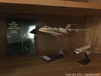 Two airplane models on display stands alongside the aviation book. The larger model has a stand label 107/167.