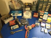 Overview of hardware items on table including stapler, tape, rope, and boxes of staples alongside loose hardware.