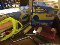 Photo showing the set of painting tools including Ready Roller box, EdgeMaster box, several paint rollers and roller frames on brown surface