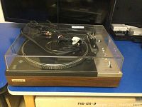Front view of Pioneer turntable with wood‐grain plinth and clear dust cover on blue table