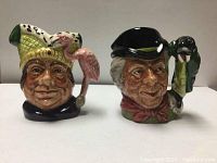 Front view of the two Royal Doulton toby jugs depicting character faces with detailed features and attached handles shaped like a bird and a walrus respectively.