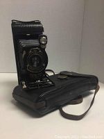 Side angle showing open camera bellows and closed carrying case below.