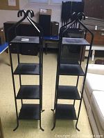 Two black wrought iron plant stands, each with four square shelves, visible front view.