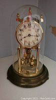 Full side view of the Kinder anniversary clock under a clear glass dome with a metal base.