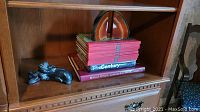 Shelf showing a stack of books including The Century, The Canadian Centennial Library, Rand McNally Cosmopolitan World Atlas, Great Canadian Writing series, and a bronze-colored Wolf Original sculpture beside them.