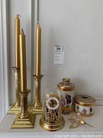 Small anniversary clock under a clear glass dome featuring gold metal details and internal figurines, alongside two decorative porcelain vessels and a gold hummingbird figurine.