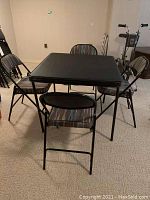 Card table with four folding chairs around it on carpeted floor.
