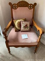 Front view of wooden armchair with carved backrest, pink upholstery, and two decorative cushions on seat.