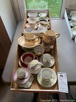 Wide view of a box containing multiple cups, saucers, creamers, and a sugar bowl with floral and decorative patterns