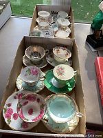Box holding an assortment of thirteen cups and saucers showing various floral patterns and gilt edges