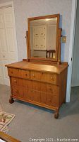 Front view of wood dresser and matching wooden-framed tilt mirror showing drawer configuration and mirror tilt supports.