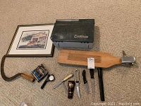 Overall view of fishing related tools, tackle box, knives, scaling board, hand cycle, and framed picture.