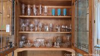 Three wooden shelves inside cabinet filled with assorted glassware and crystal items including bowls, salt and pepper shakers, various stemware and tumblers.