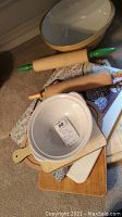 Overall view showing ceramic mixing bowls, wooden rolling pins with green handles, cutting boards, and placemat stacked together.