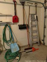 Wide shot showing all items including ladder, shovel, rakes, hoses, cultivator, and hedge trimmer in garage setting