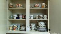 Wide view of cabinet containing Wedgwood dishes, various mugs including floral and bear themed, plates, cups, and teapot.